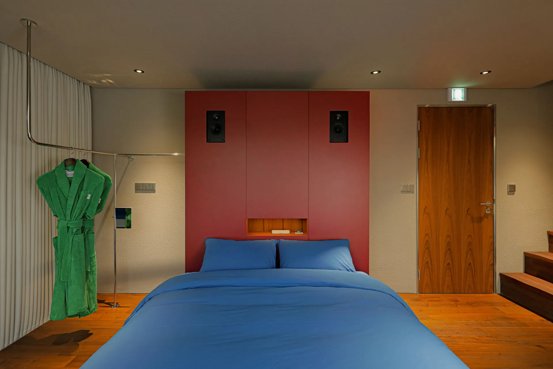 A modern bedroom with a blue and green bed, wood floor, and wooden door.