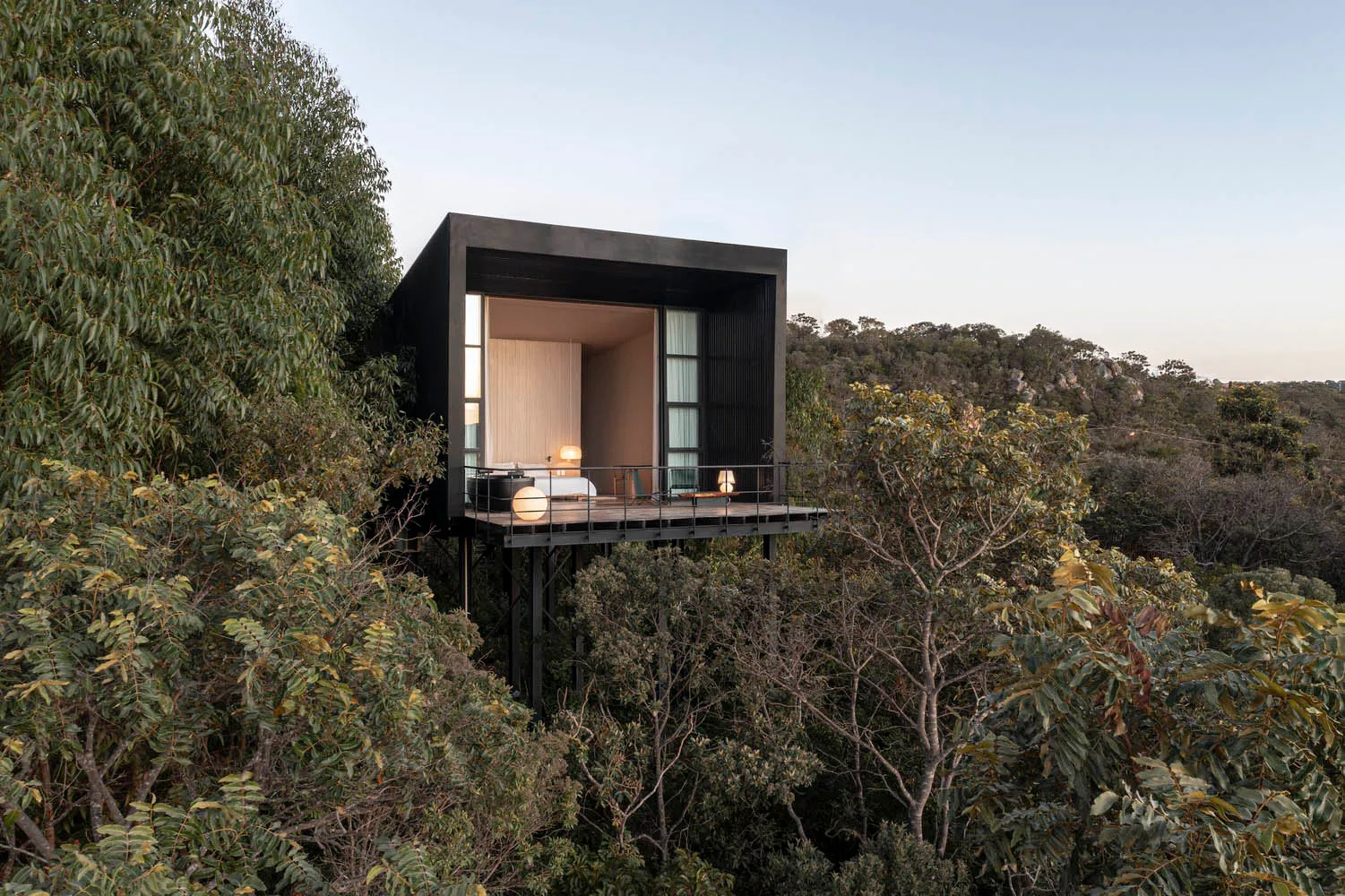 Minimalist, modern treehouse residence with black exterior and white interiors, elevated on stilts over dense forest.