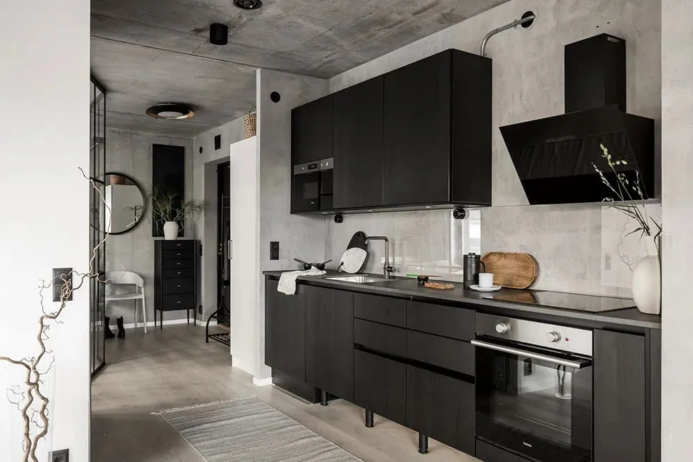 A contemporary kitchen with black cabinets, concrete walls, and wood accents, featuring a modern kitchen sink, open floor pla