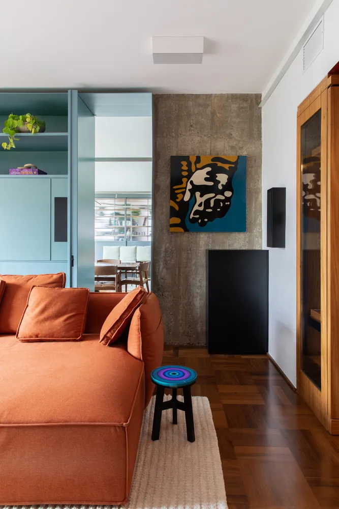 A modern industrial living room showcasing concrete, walnut, and orange sofa, with a concrete accent wall and wooden flooring