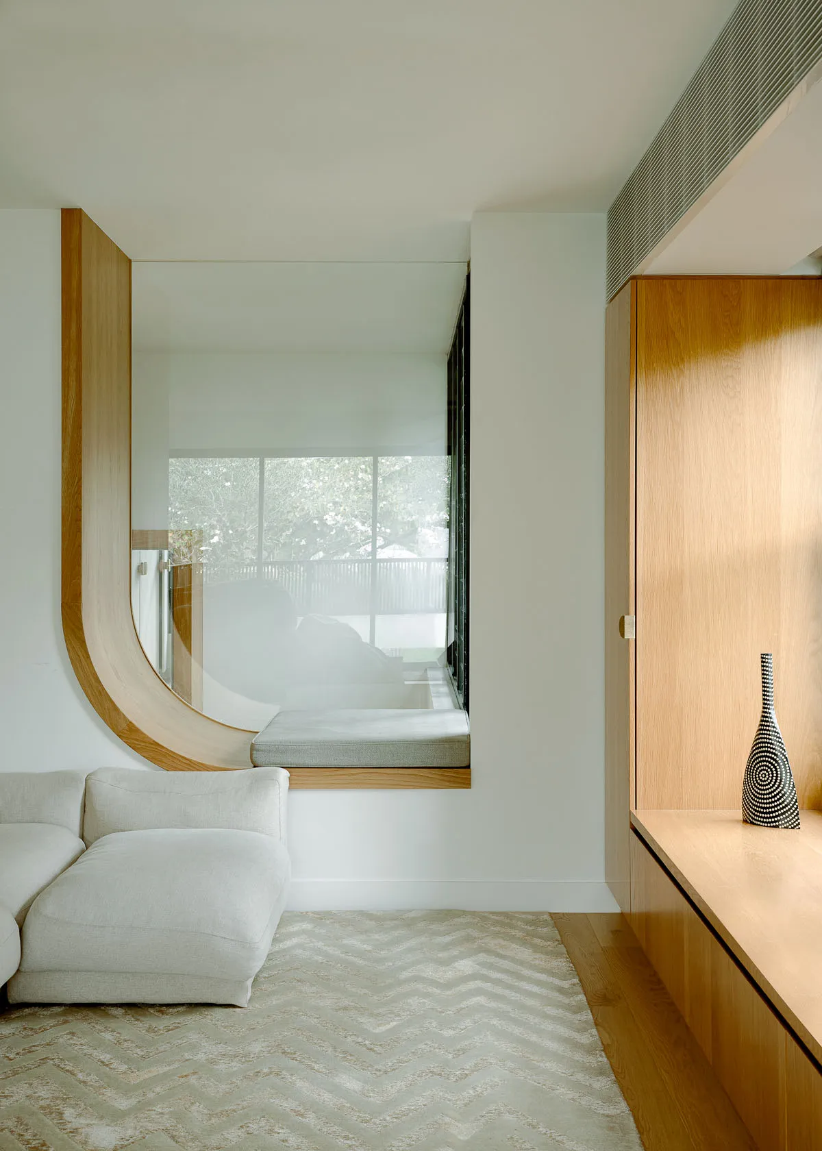 Modern living room with white sofa, wooden shelves, and window seat