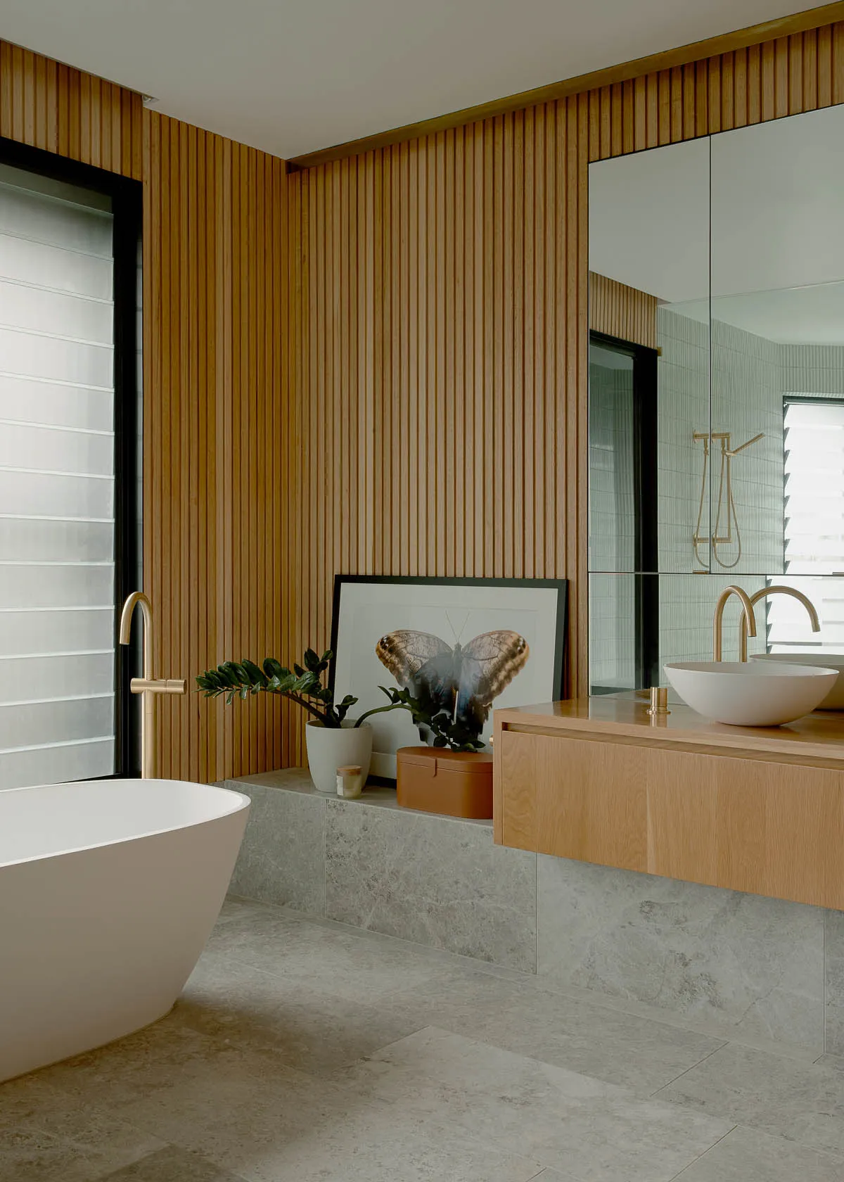 A modern minimalist bathroom featuring wooden walls, a freestanding tub, and a floating vanity with a round vessel sink and b