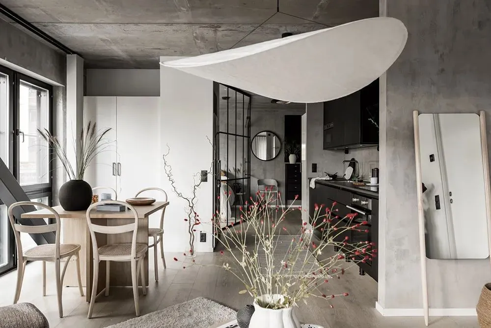 A modern living room, dining room, and kitchen with concrete walls and wooden furnishings.