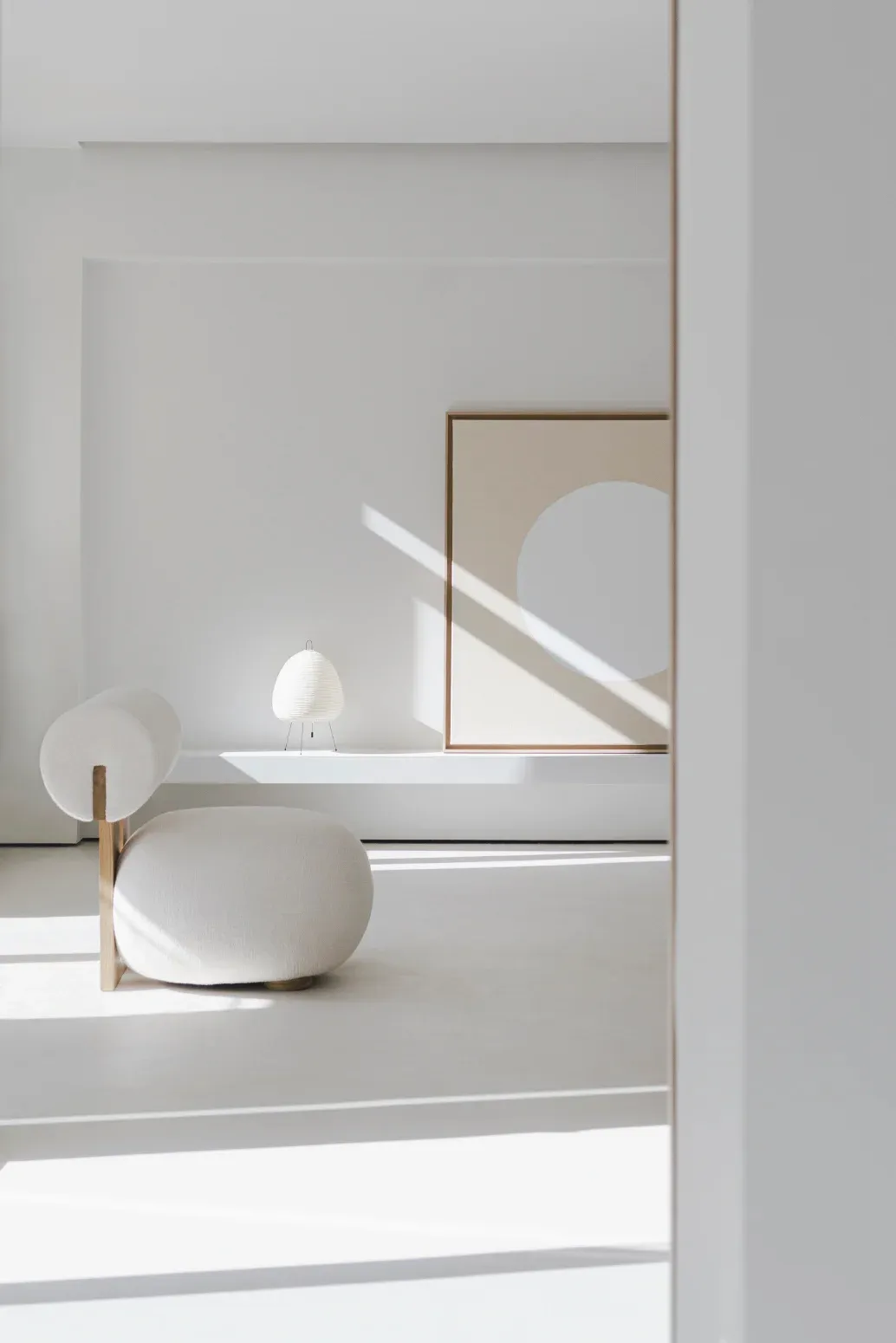 Modern minimalist living room with a white upholstered chair and a white lantern lamp on a white shelf.