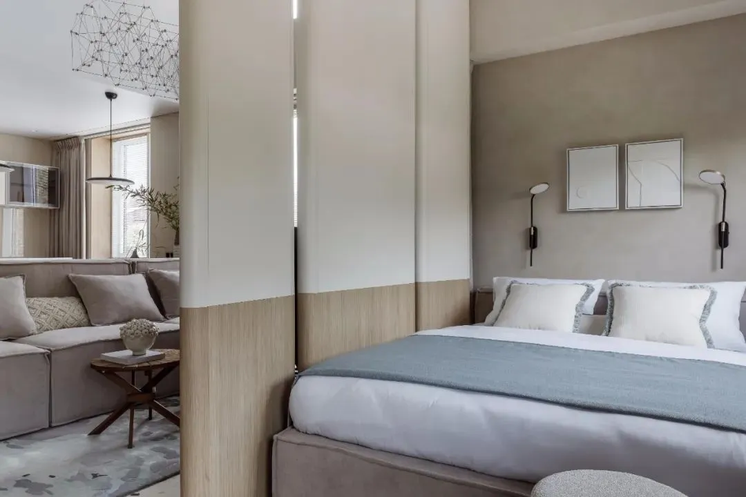 A minimalist bedroom with neutral tones and textured surfaces, featuring a bed with two headboards and a sofa in the backgrou