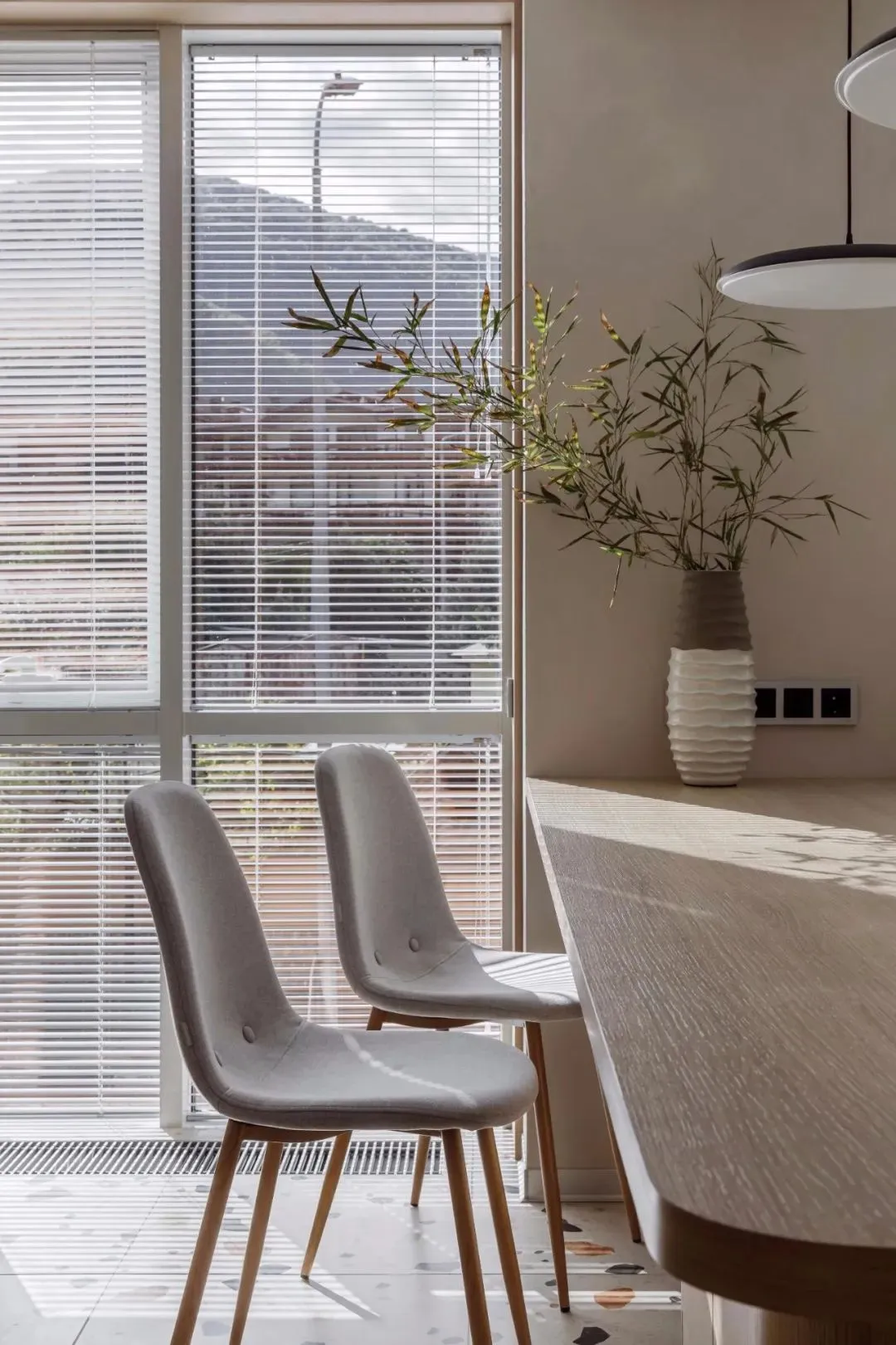 Two minimalist grey chairs sit at a dining table with a vase of greenery in a modern interior design living space.