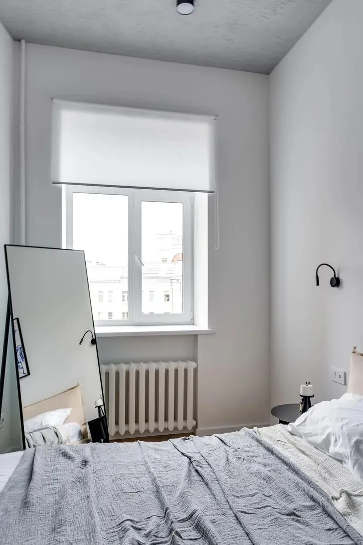 A minimalist bedroom featuring light-colored materials and a gray bedspread.