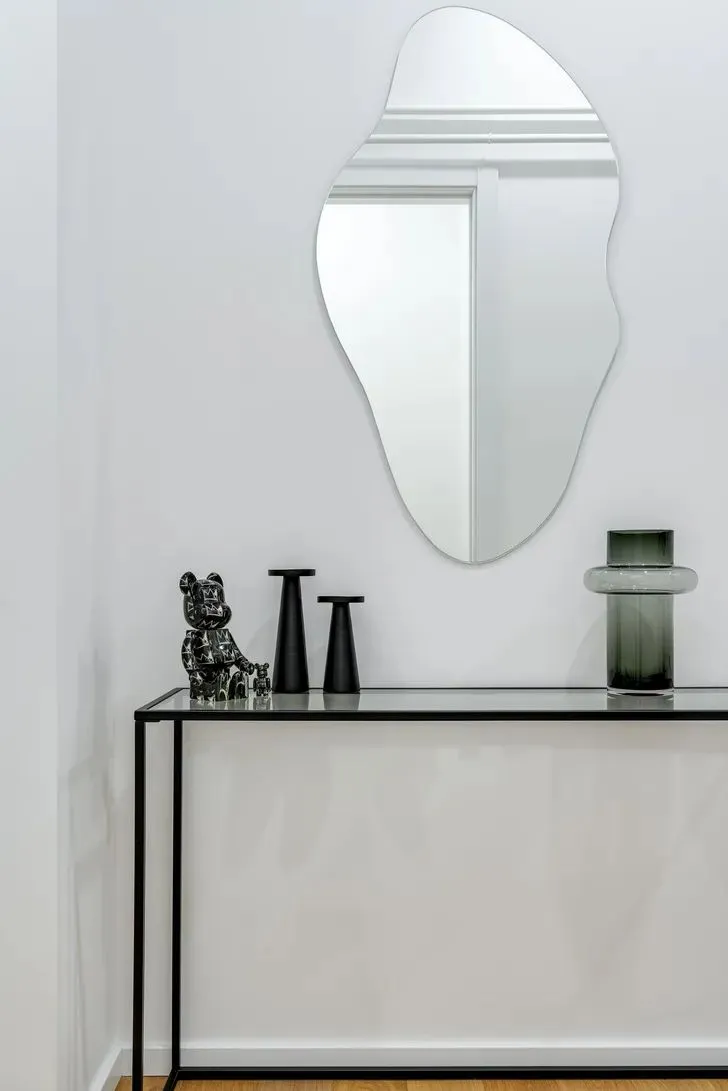 A minimalist console table displaying modern decor items, including a glass vase, a black bear figurine, and two black candle