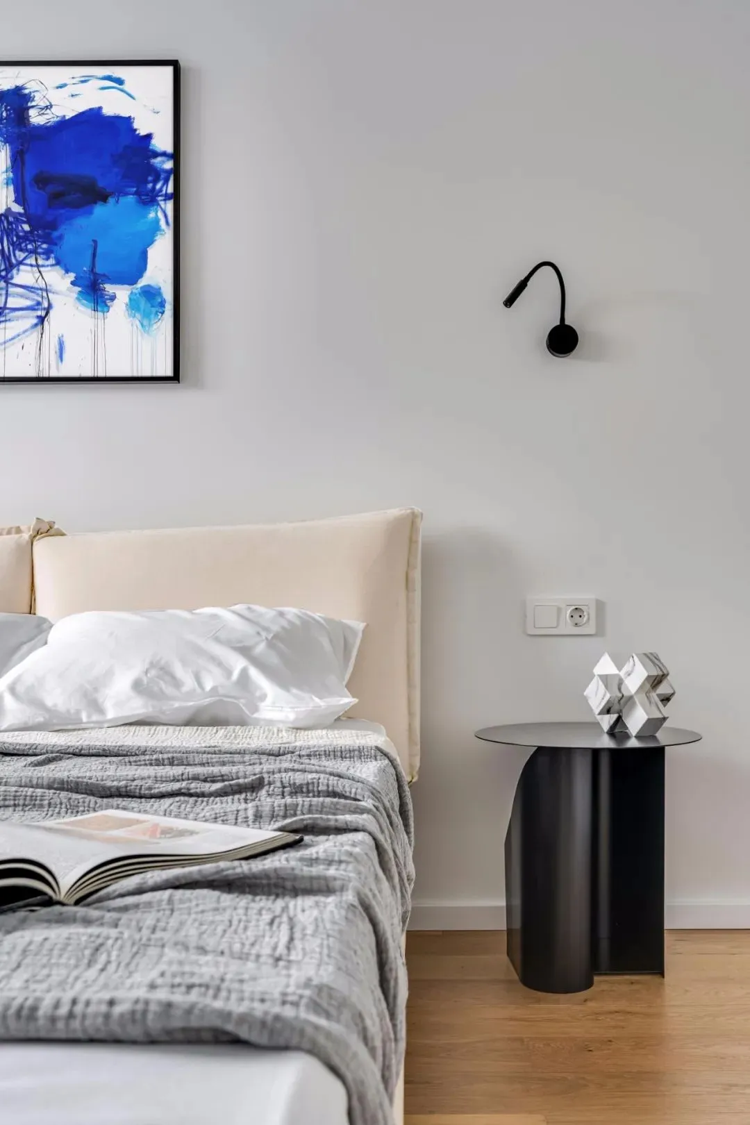 A modern bedroom with a beige bed and a metal side table with a geometric sculpture on top.