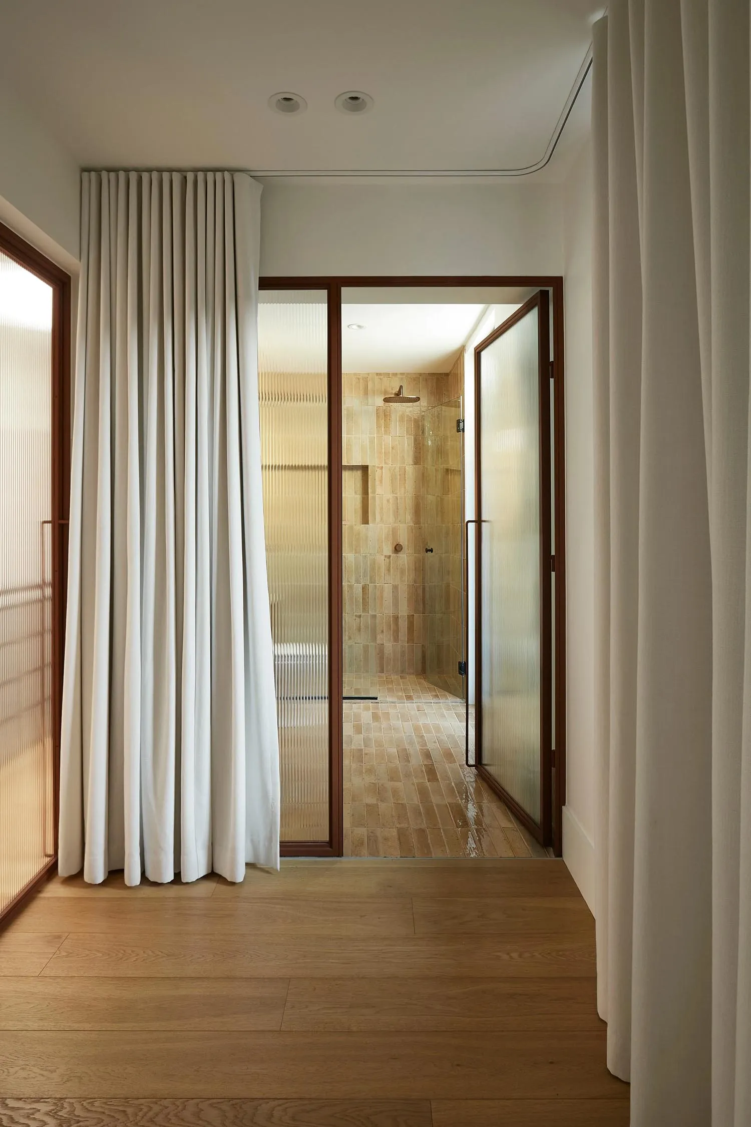 A minimalist bathroom with tiled walls and floor, featuring a frosted glass partition and a metal-framed glass door.
