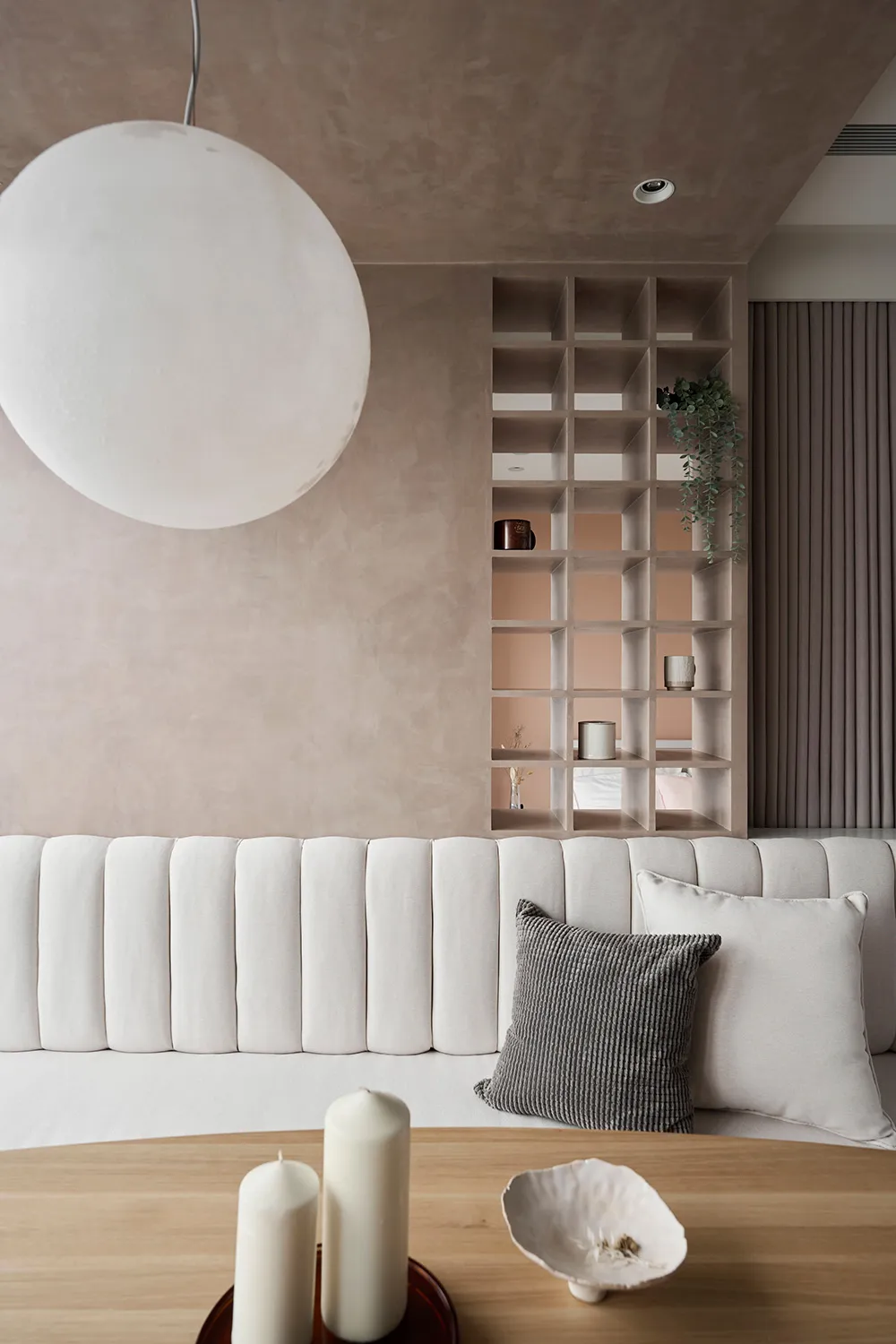 A minimalist living room with concrete walls, a white sofa, and a wooden coffee table with candles and bowls.