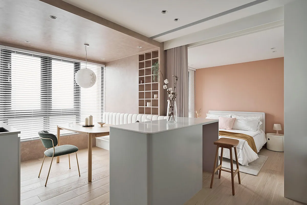 A modern, minimalist kitchen with white countertops, wooden chairs, and a white pendant light hanging from the ceiling.