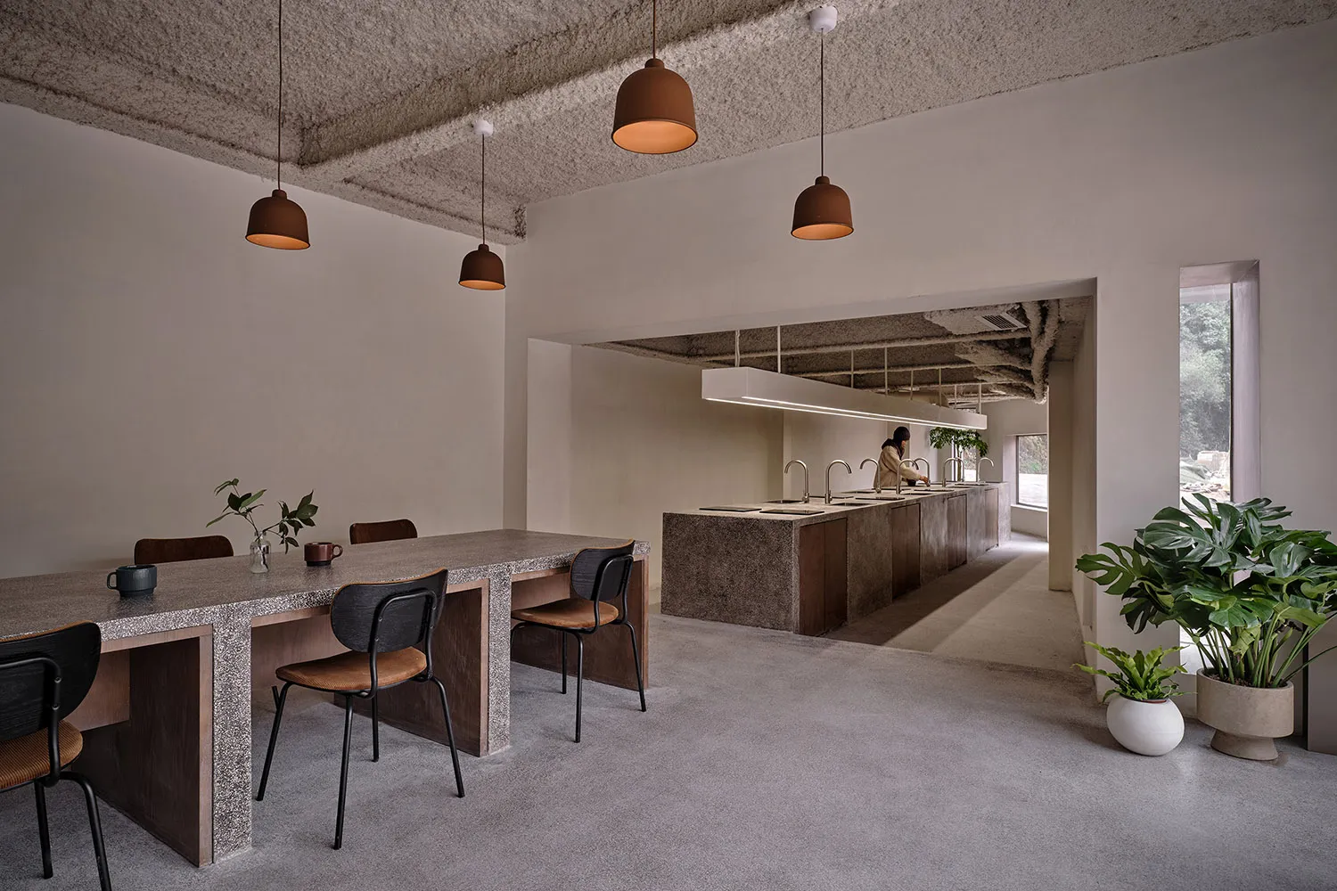Minimalist cafe interior with concrete walls, wood furniture, and hanging pendant lights.