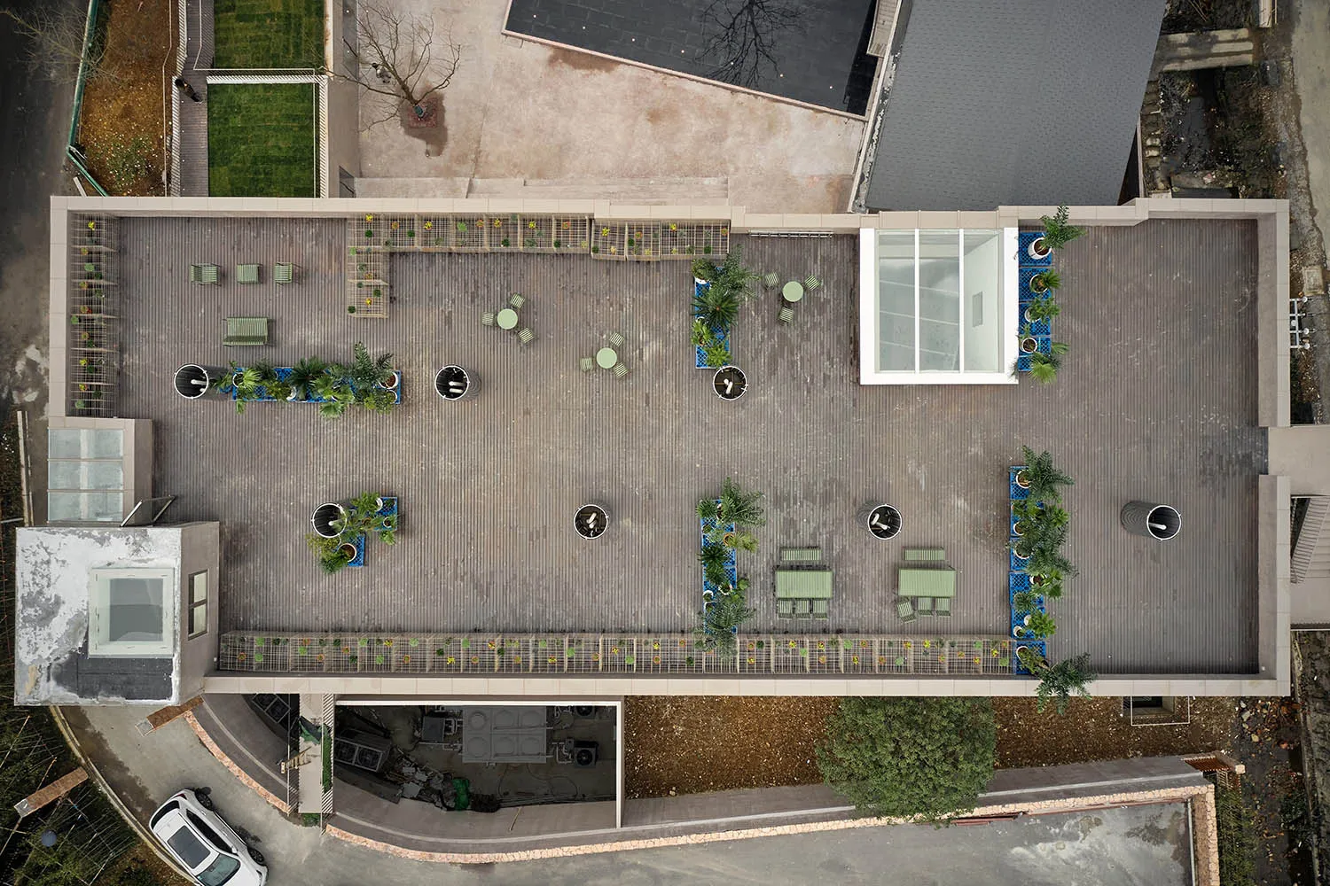 Aerial view of a modern wooden patio with potted plants, outdoor furniture, and a transparent glass wall.