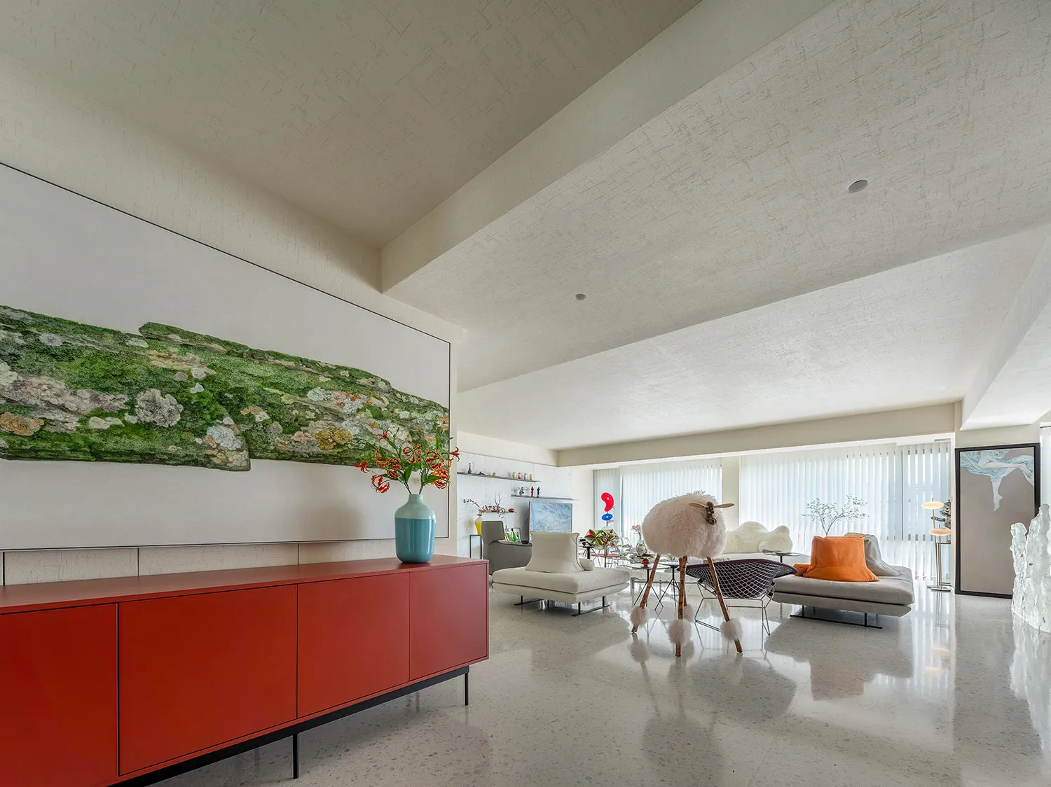 A modern living room with a red sideboard, white sofas, and a large green wall art piece.