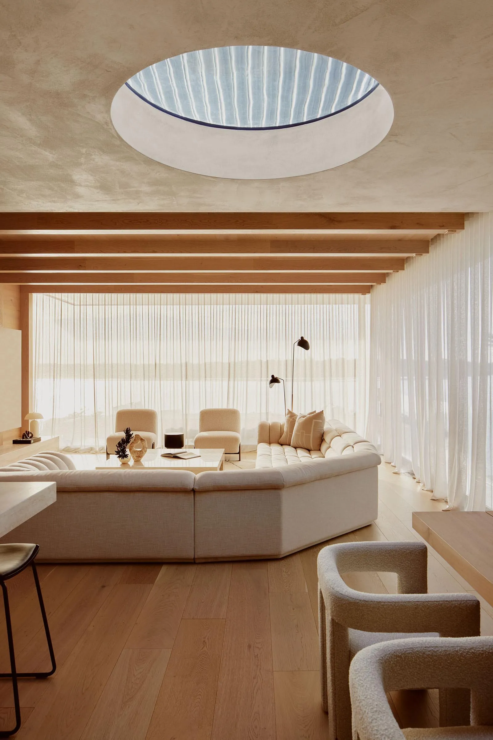 A minimalist modern living room featuring a circular skylight, a long sectional sofa, and wooden floors.