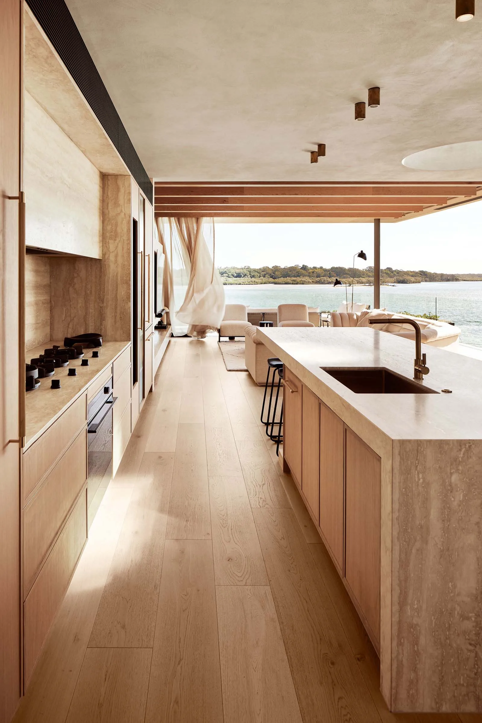 A modern residential kitchen featuring wooden cabinets, a marble countertop, and a view of the ocean.