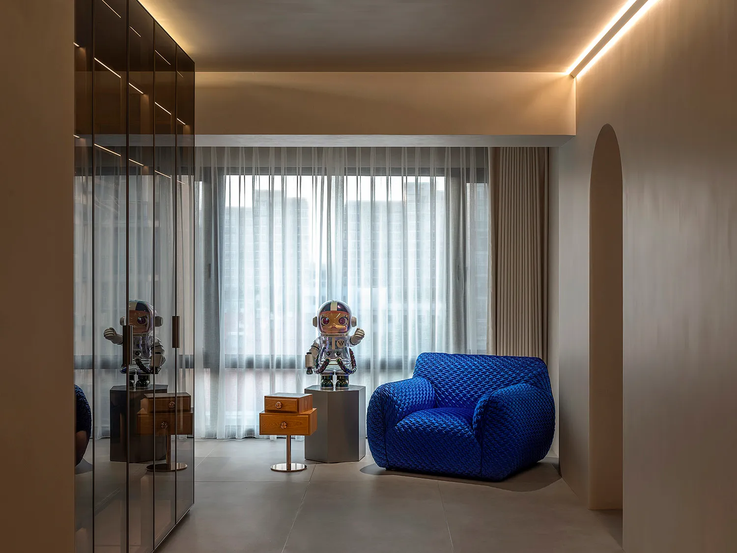A modern blue armchair with a textured upholstery in a room with large windows and sheer curtains.