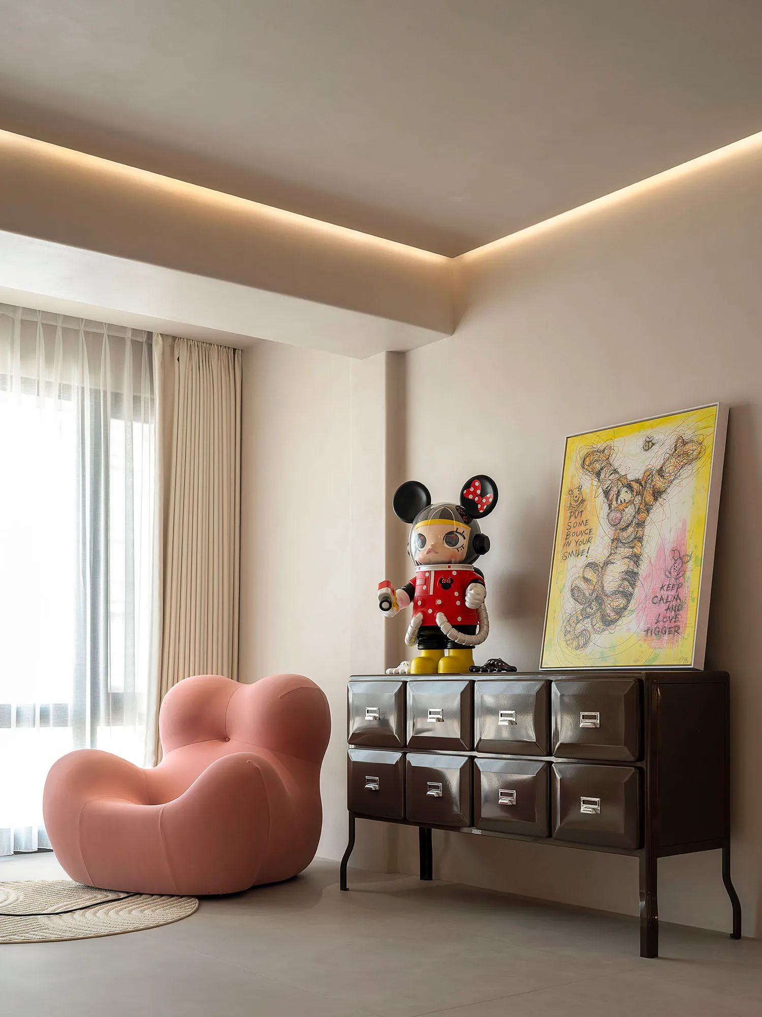 A modern living room featuring a pink cushion and decorative elements such as a cabinet with drawers, a framed picture, and a