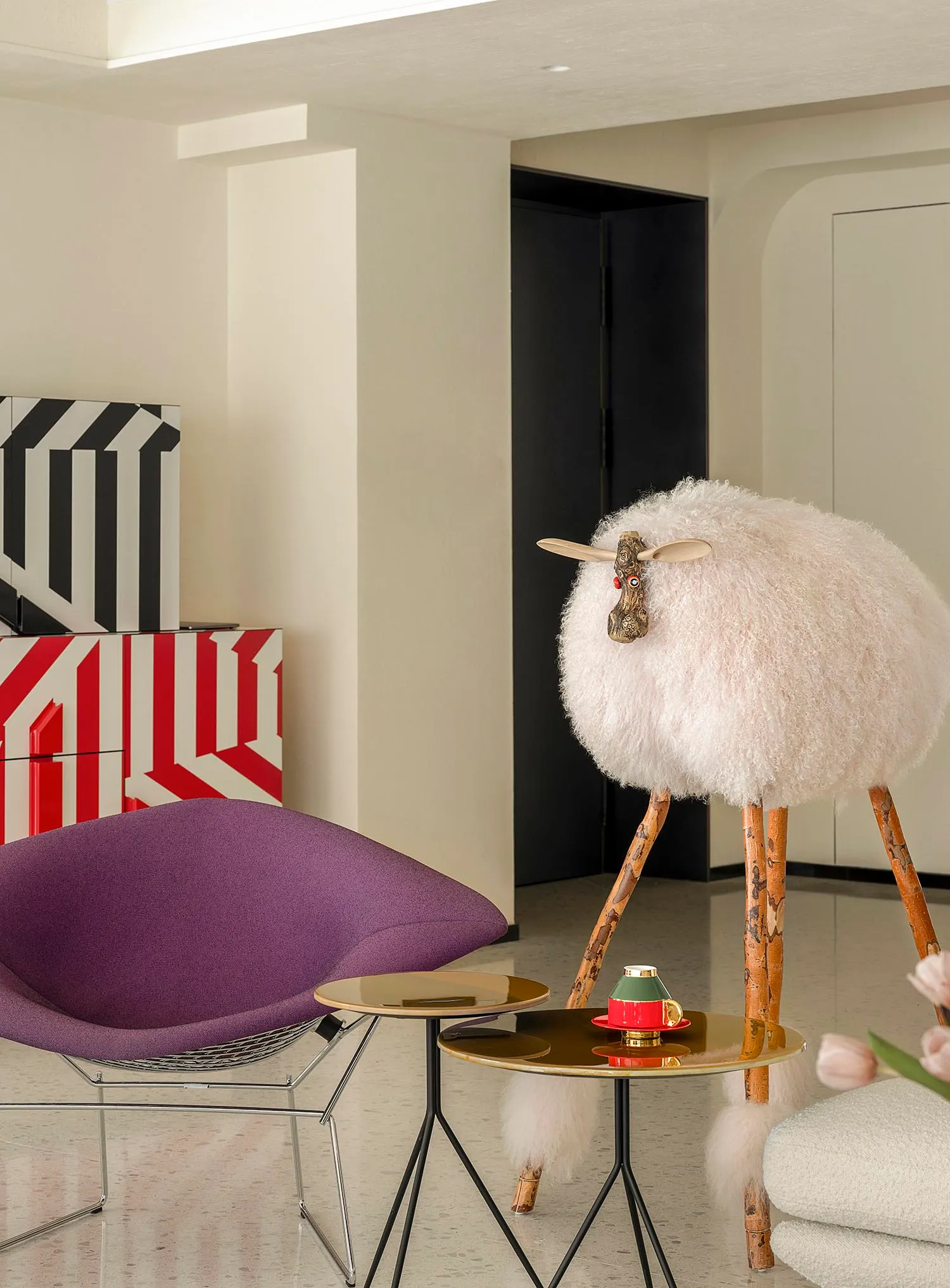 A modern living room with a purple fabric chair, a sheep sculpture, and a side table with a coffee cup and vase of pink tulip