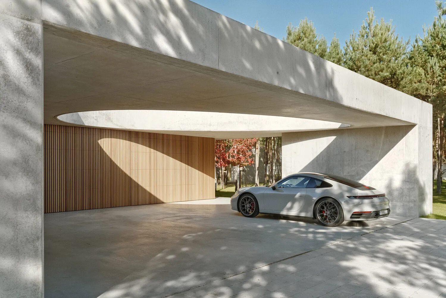 White Porsche parked in a minimalist, modern, concrete carport with wood accents.