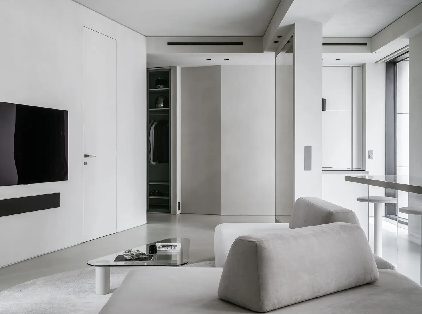 A modern minimalist living room with concrete walls, a grey sofa, and a glass coffee table.