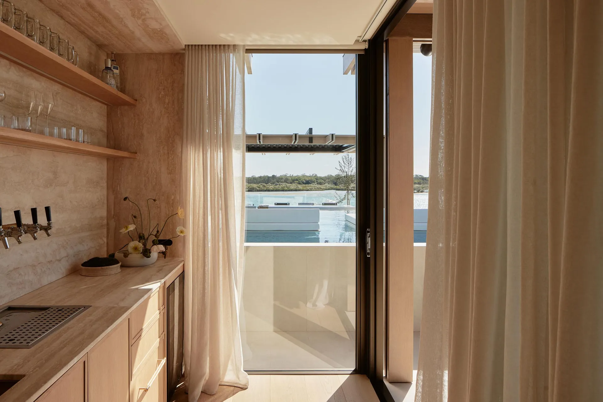Modern residential home interior with neutral materials and a view of the pool and outdoor area.