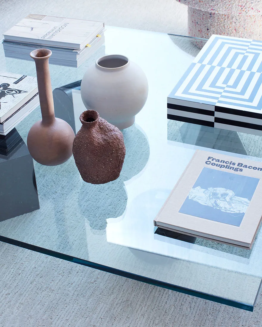 A modern coffee table featuring glass and ceramic vases and books.