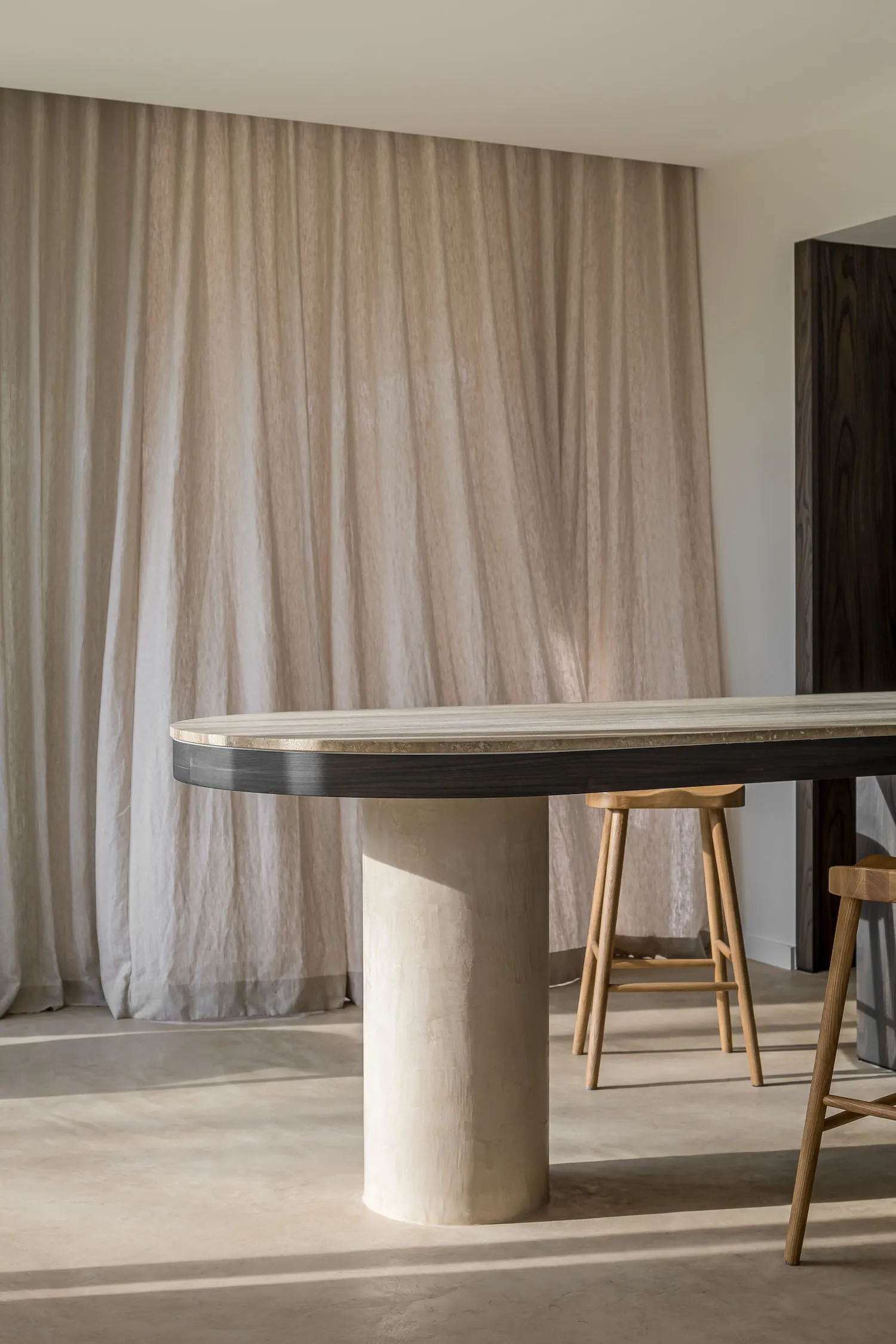 A minimalist lounge area with a textured concrete table and wooden stools.