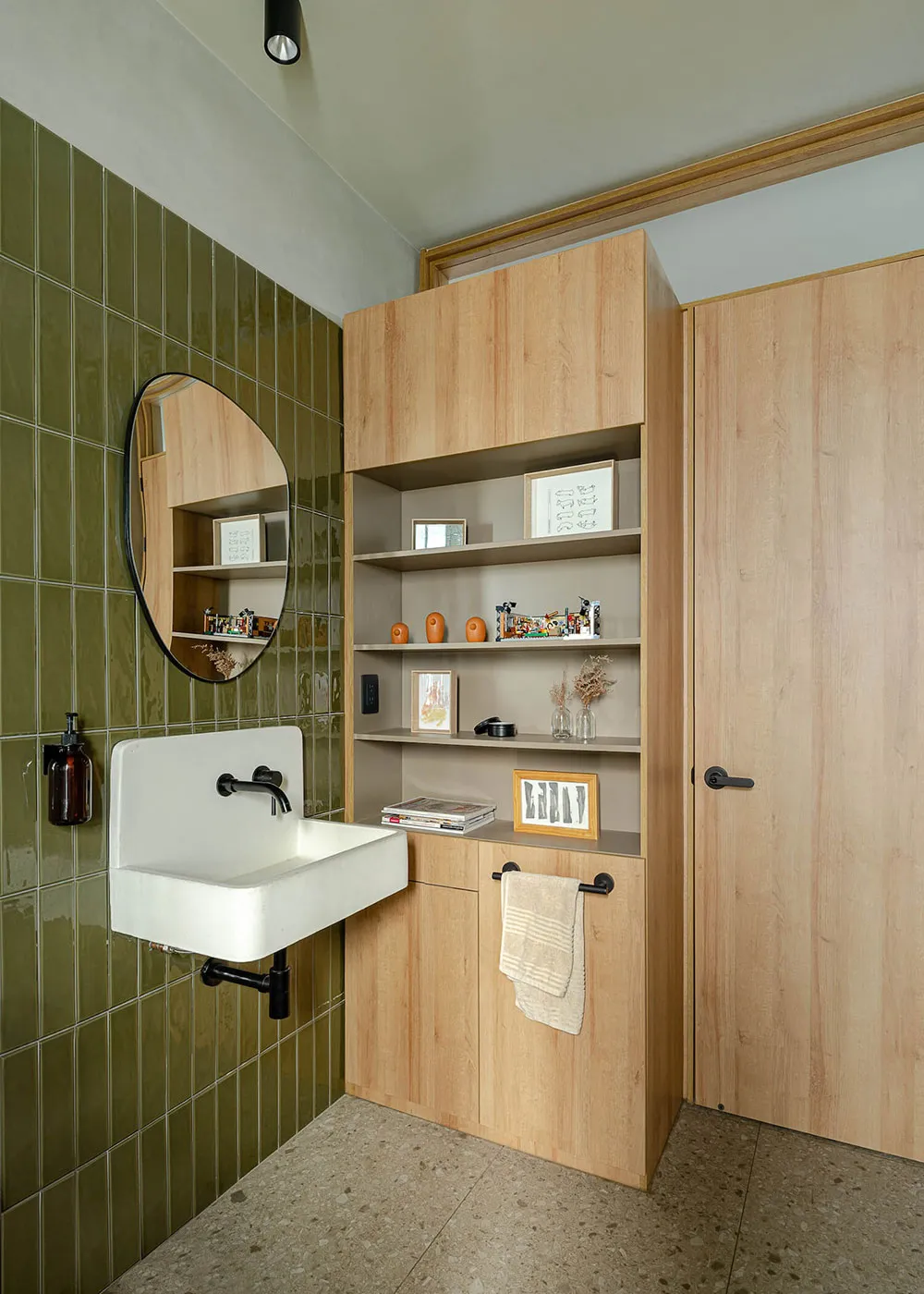 A modern bathroom featuring green tiles on the walls, wooden cabinets, and a white porcelain sink.