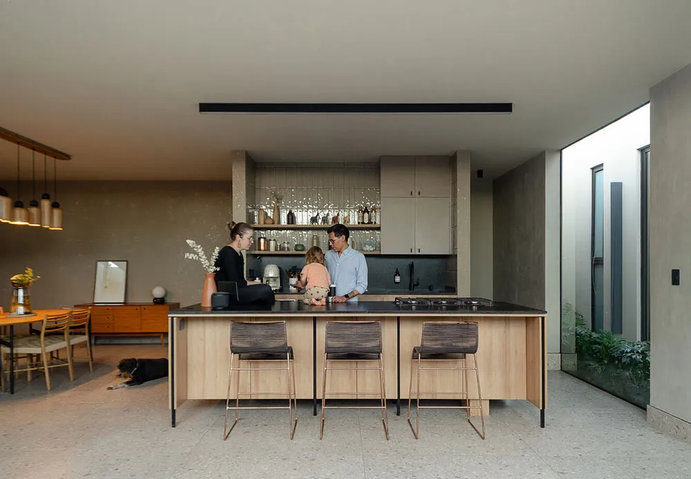 A modern family kitchen featuring concrete and glass materials with a focus on natural lighting and organic shapes.