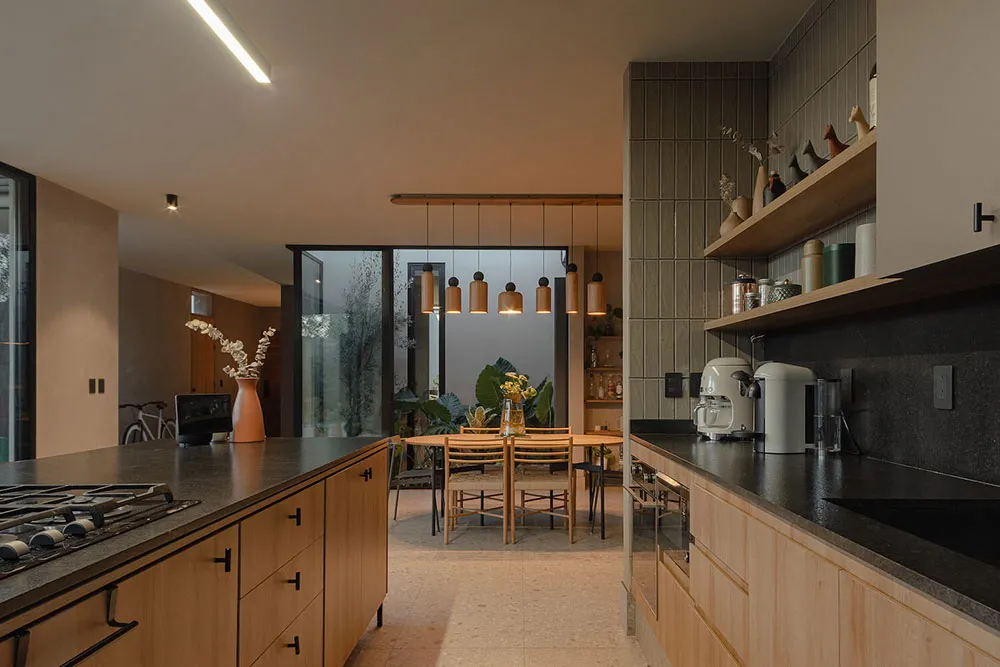 A modern residential kitchen featuring light wood cabinets and a stone countertop with pendant lights hanging above an island