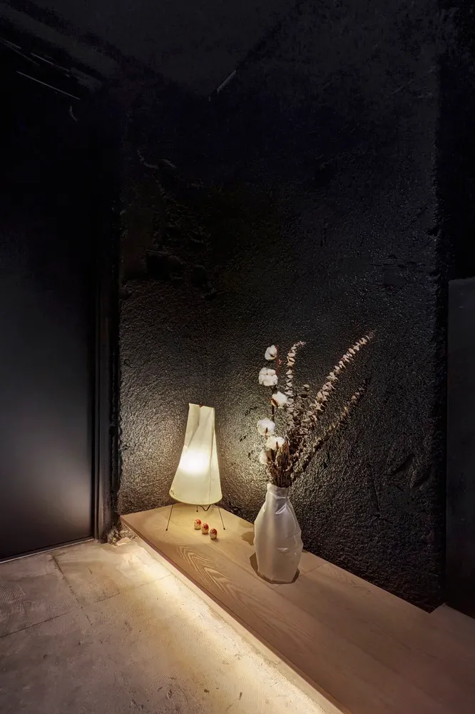 A minimalist interior design featuring light wooden furniture and fabric lamp in a dark room setting.