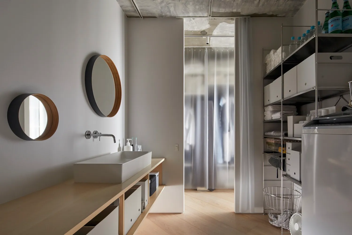 A minimalist laundry room with tall steel shelves, wood cabinetry, and a sink.