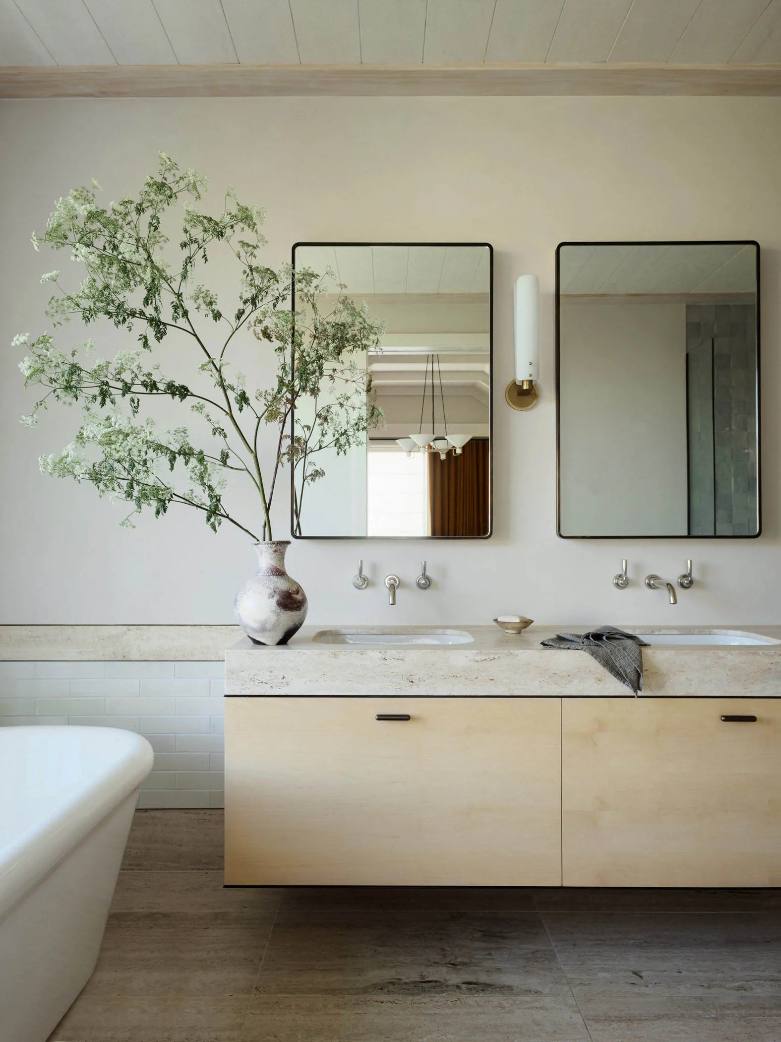 A modern bathroom featuring a floating wooden vanity counter with a stone countertop, dual sinks, and a large vase with green
