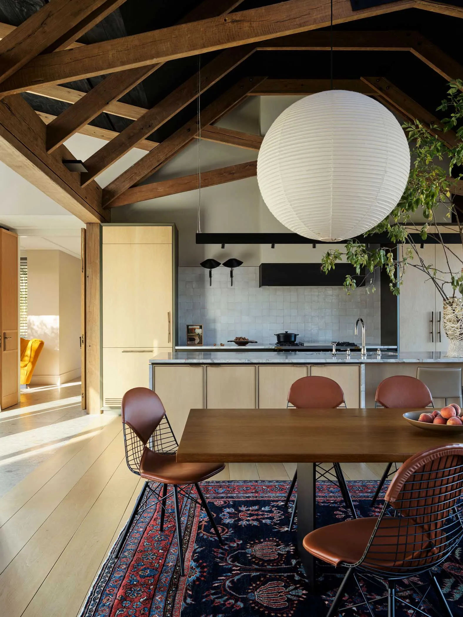Modern kitchen and dining room interior with wooden table, leather chairs, metal accents, and wooden beams