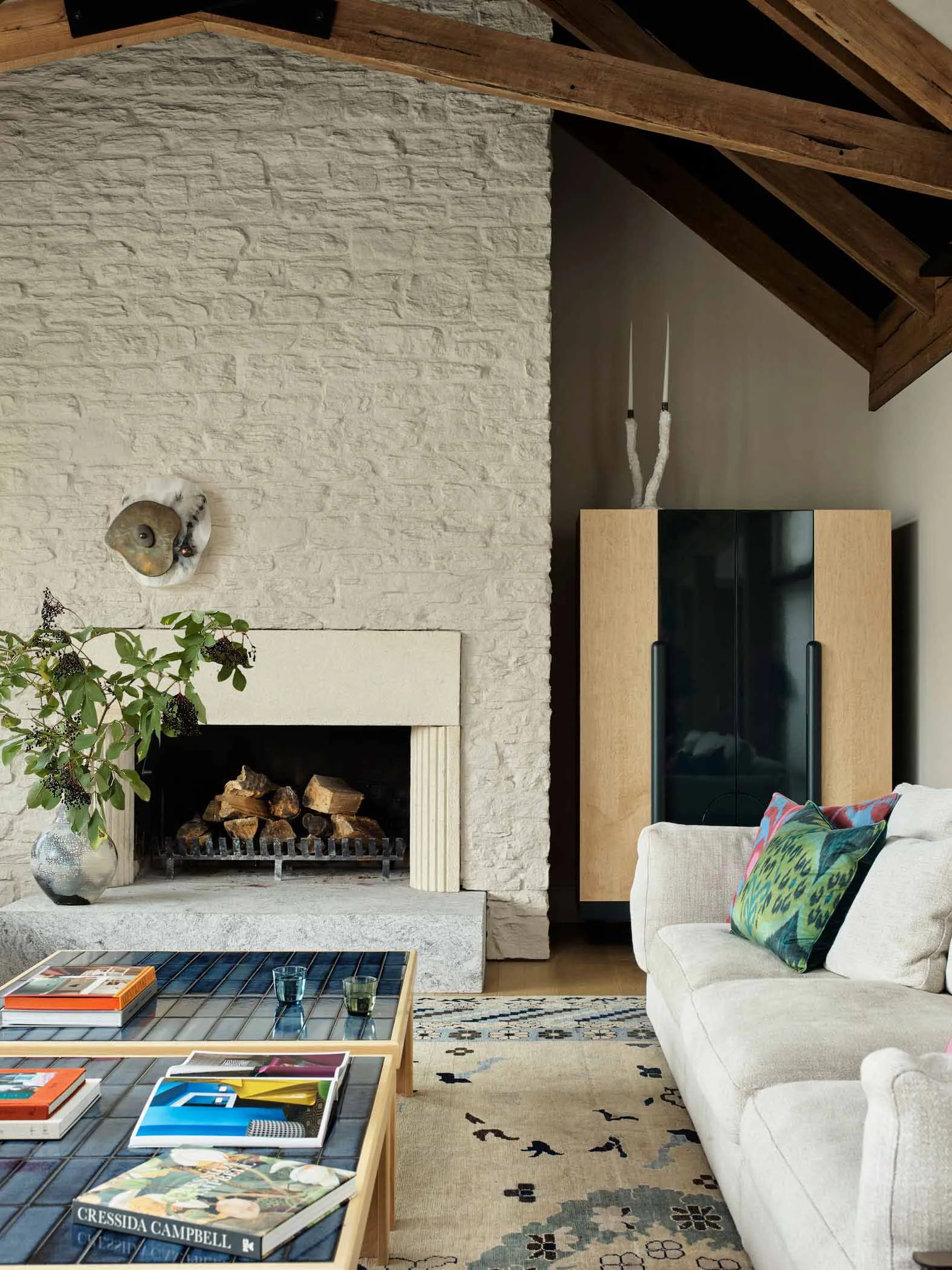 Modern living room featuring a comfortable sofa, a stone fireplace with wooden beams, and a coffee table with books and magaz