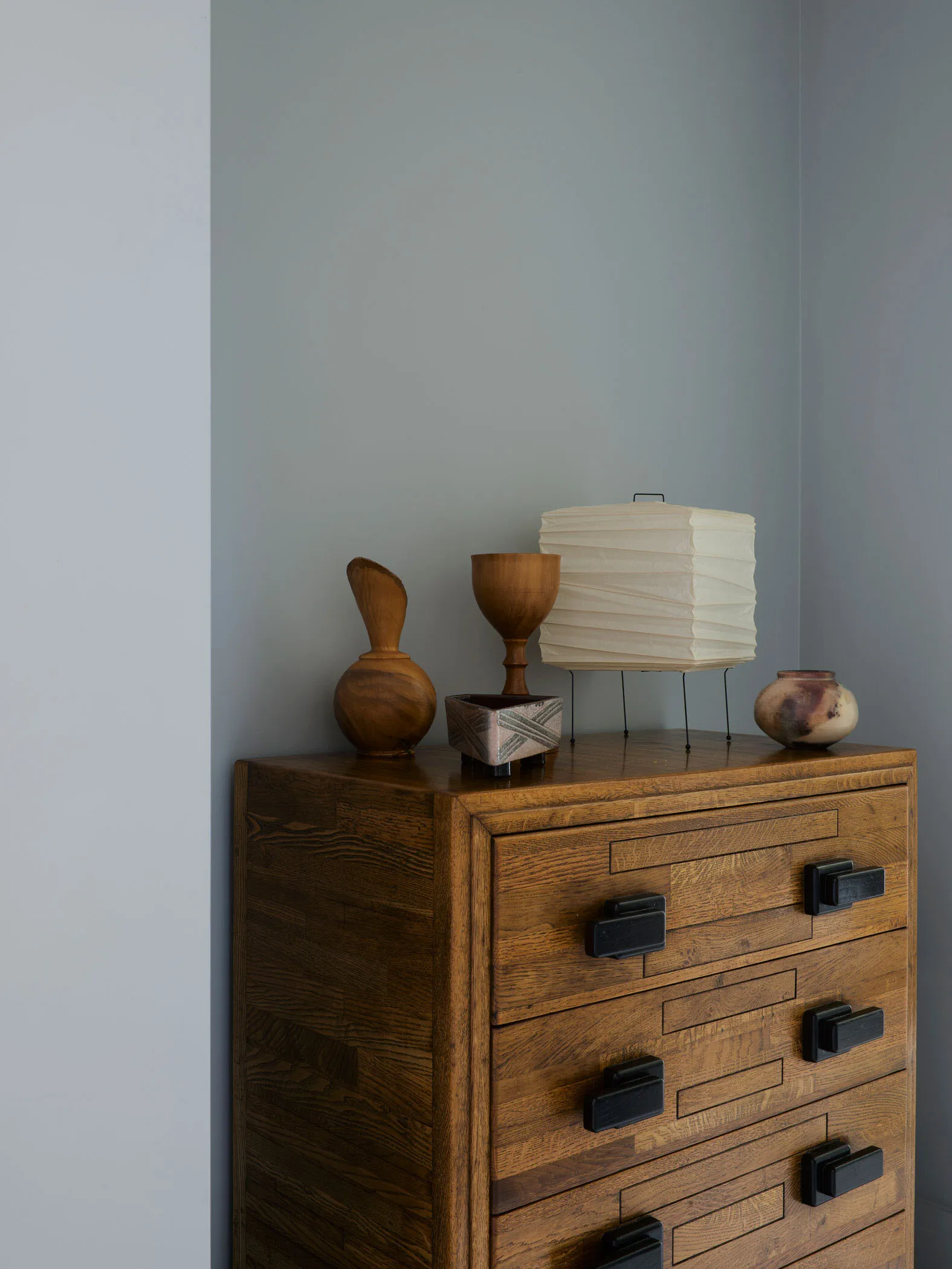 A wooden sideboard with minimalist design features, including a series of drawers with black handles and decorative objects o