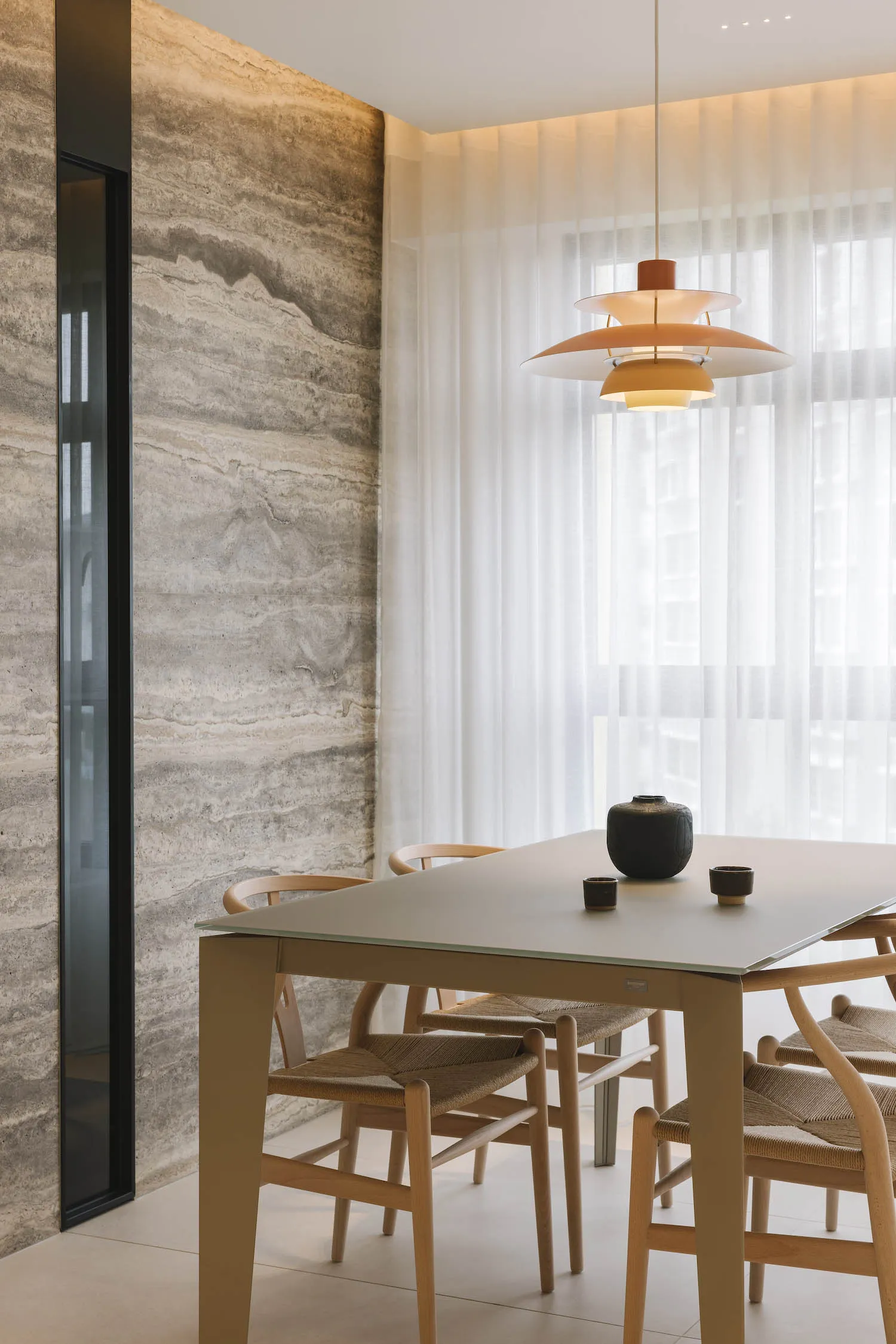 A modern dining room featuring marble walls and a concrete floor with a white table and wicker chairs.
