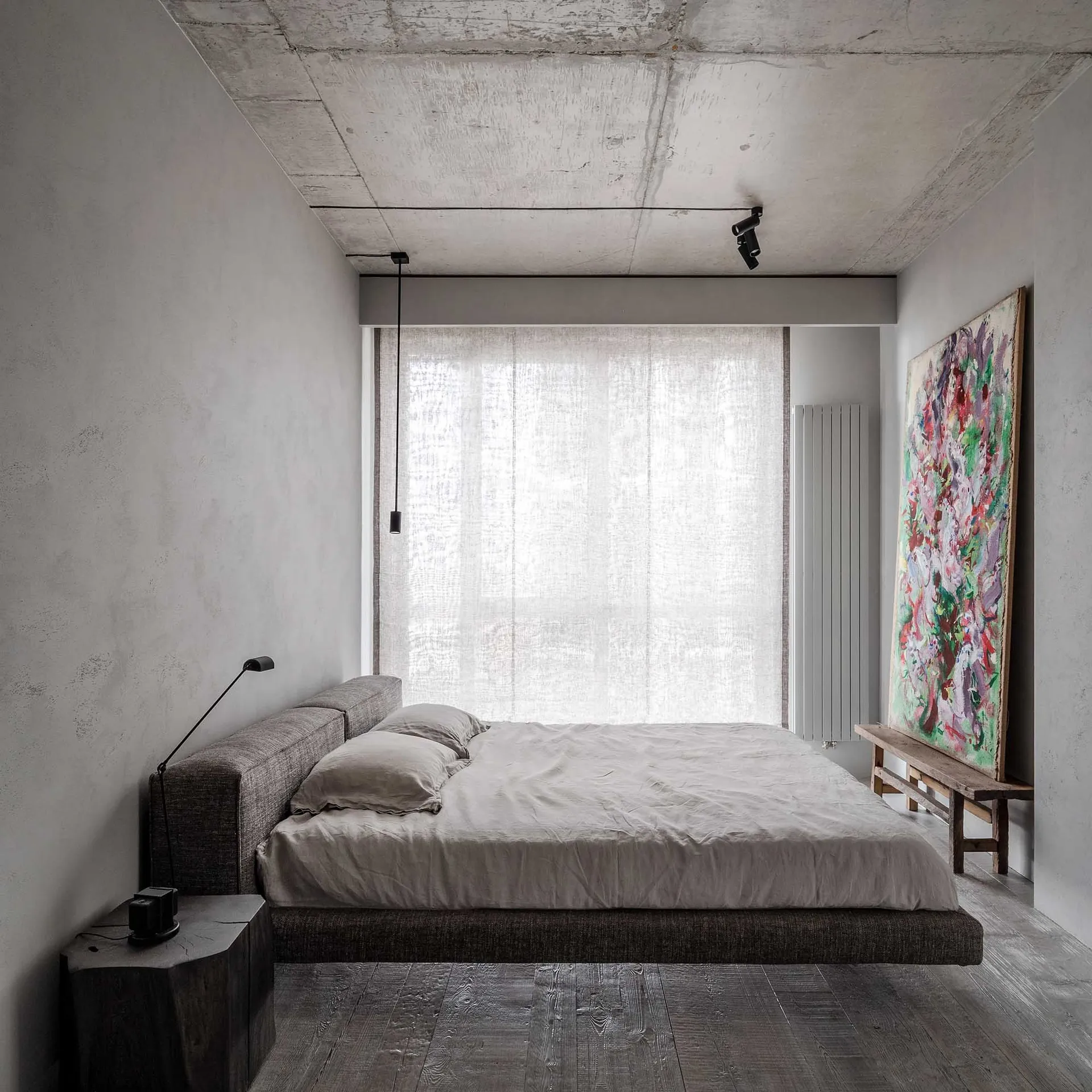 Modern minimalist bedroom with a textured concrete ceiling, large window with sheer curtains, and an abstract painting leanin