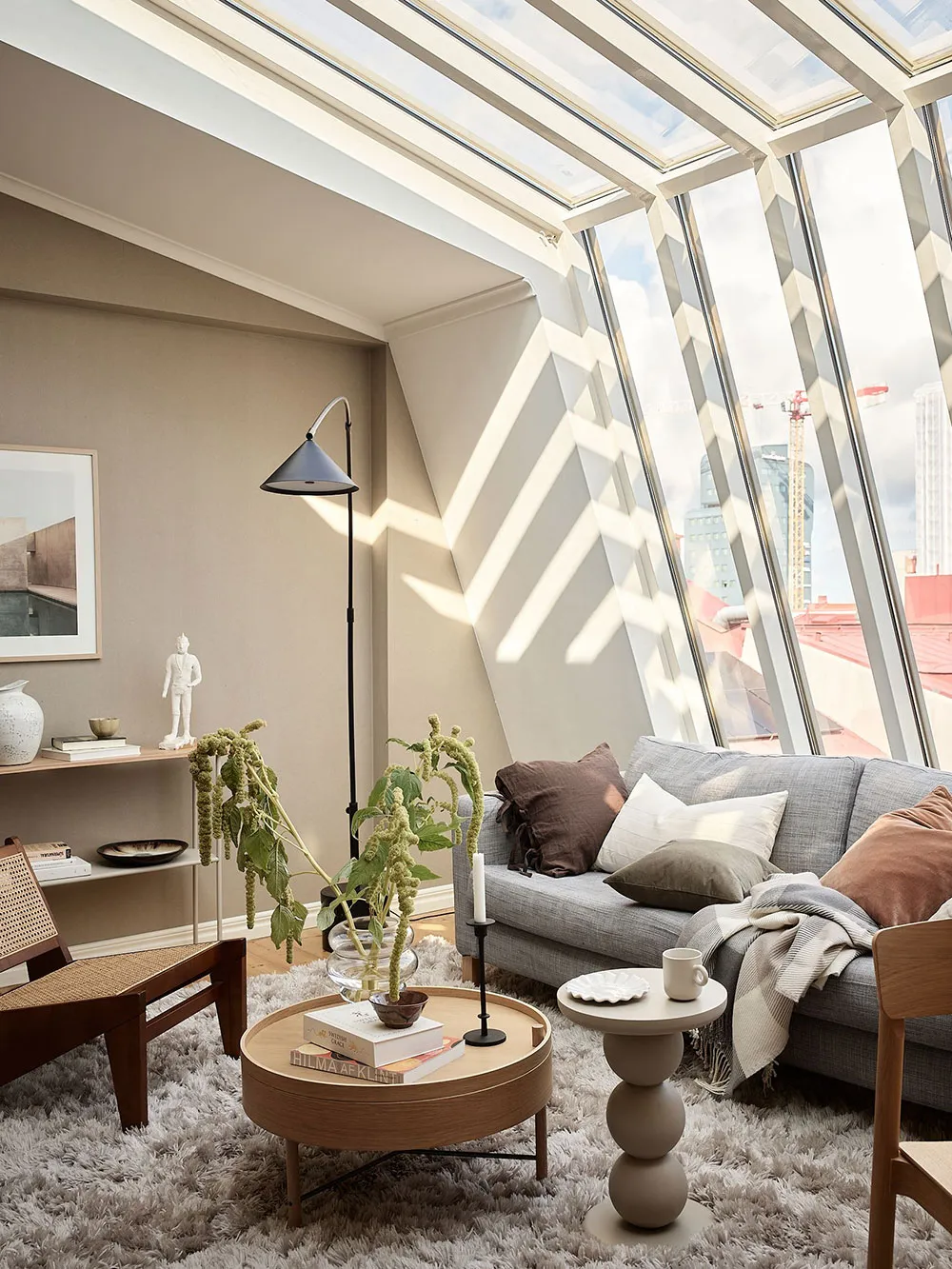 A minimalist living room with a round wooden table, floral arrangement, and white decor elements.