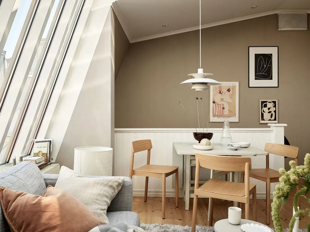 A minimalist living room and dining area with a white sofa, wooden chairs, and a dining table.