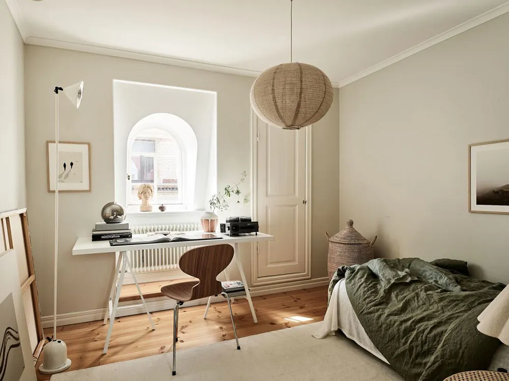A minimalist residential bedroom featuring a wooden desk, a large window, and a comfortable bed.