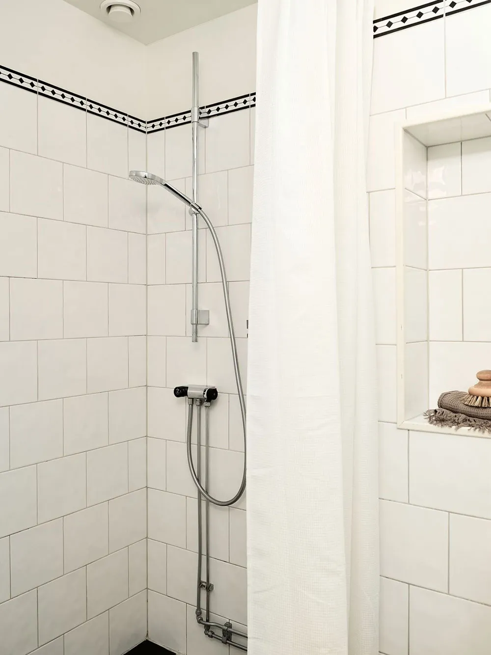 White-tiled minimalist bathroom shower area with a shower curtain and built-in niche.