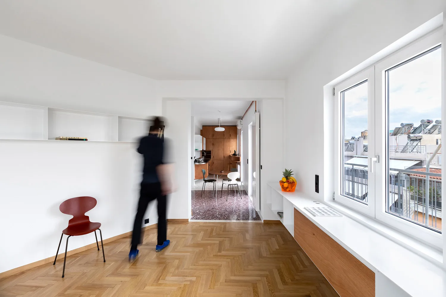A modern living room featuring wooden flooring, minimalist furniture, and a large window overlooking the city.