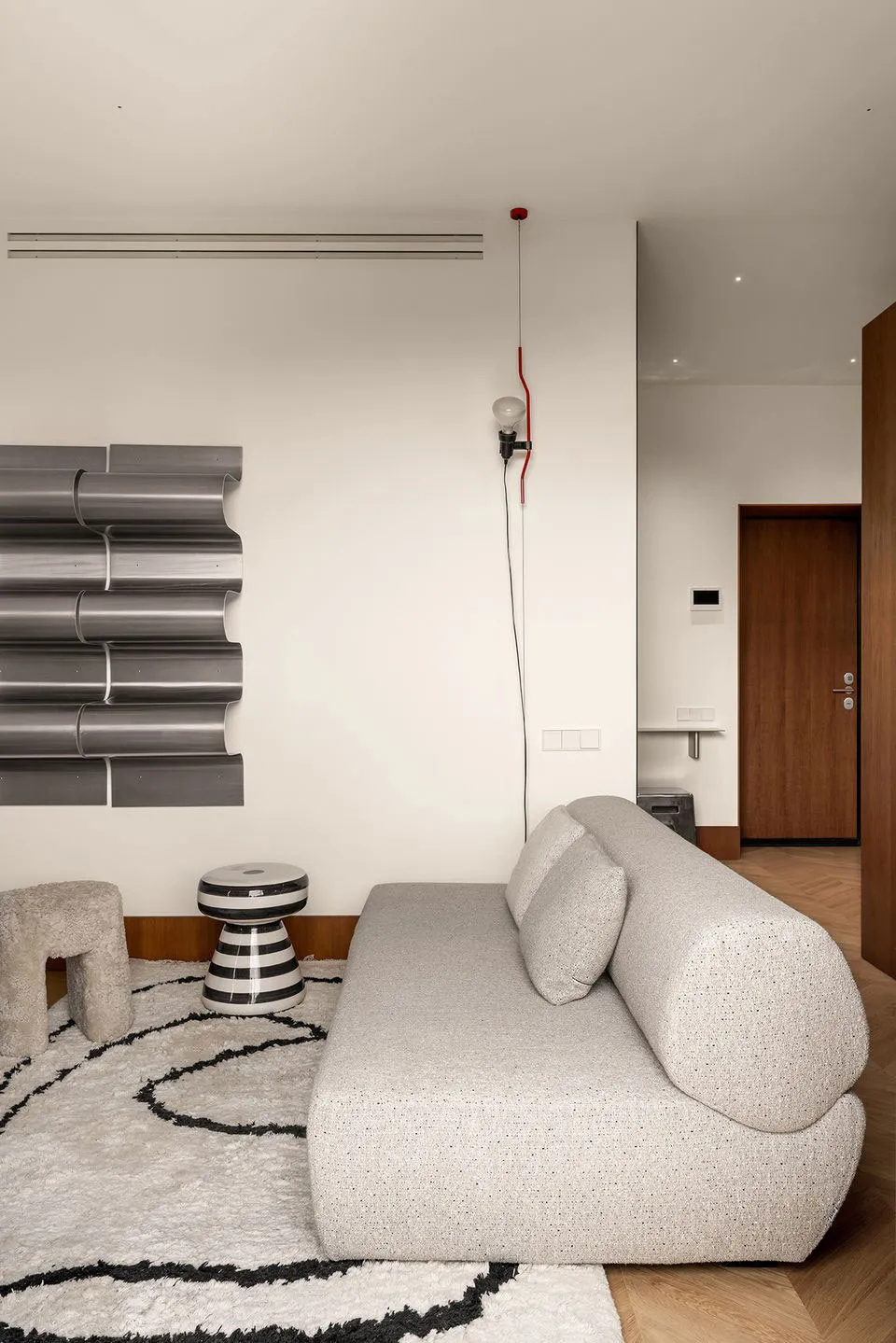 A minimalist living room featuring a grey upholstered sofa on a patterned rug, with a metallic wall art piece and a unique ta
