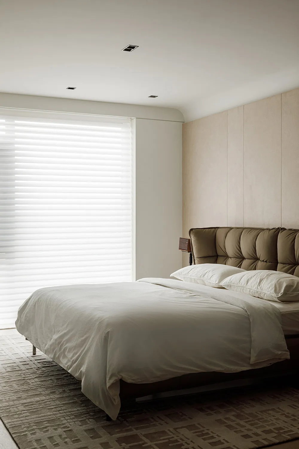 A modern bedroom with a brown leather bed, white blinds covering a window, and a white blanket on the bed.
