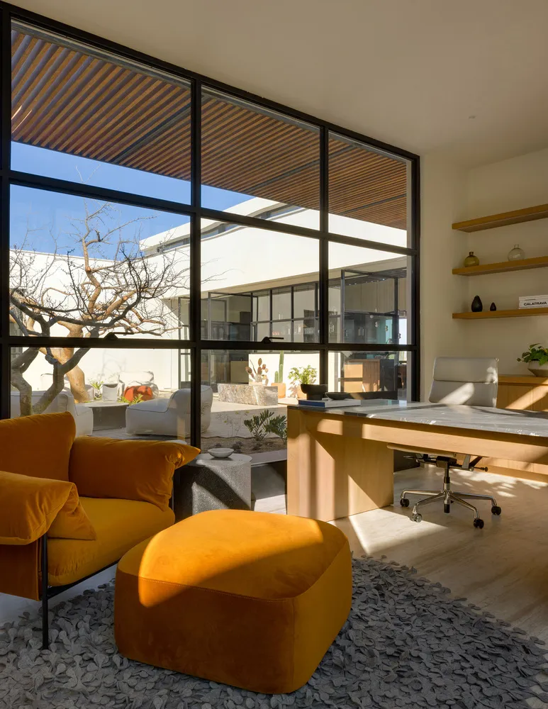 A modern home office featuring a window view with a comfortable seating area and a sleek desk.