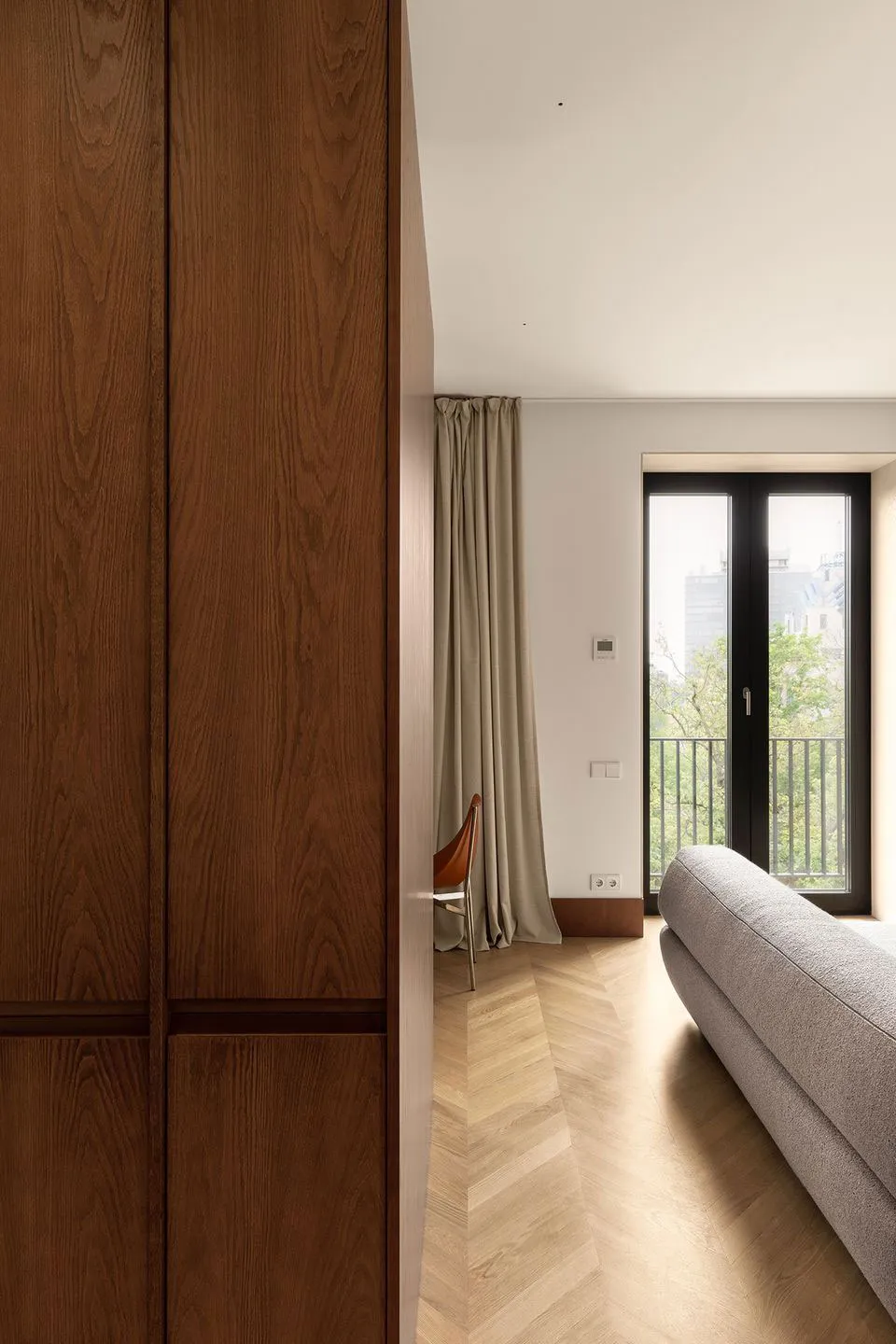 A modern living room featuring a wooden cabinet, a glass door leading to a balcony, and a gray fabric sofa.