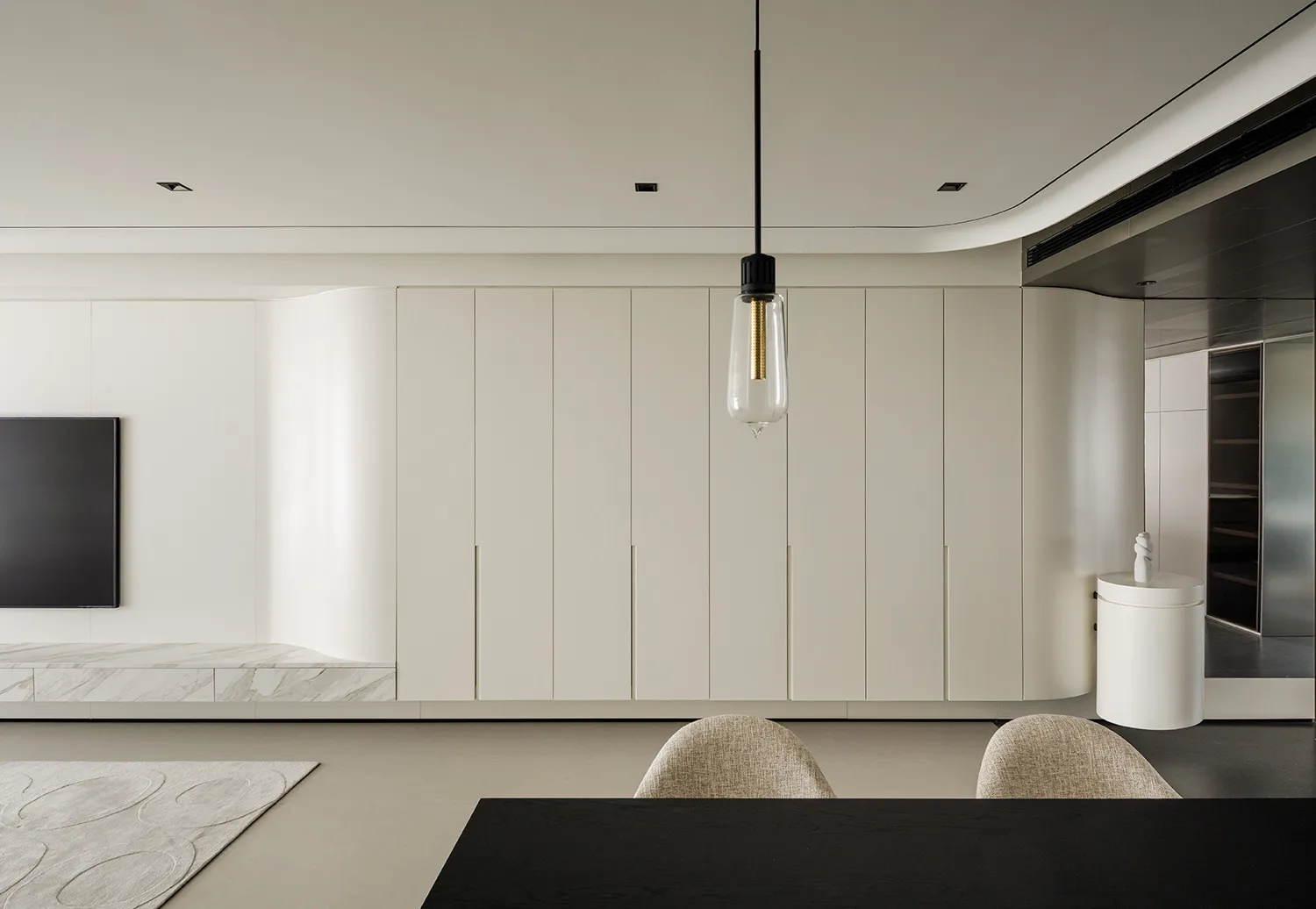 Minimalist residential interior featuring sleek, white cabinetry and a black dining table.
